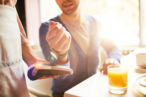 Hand of businessman with smartwatch over payment machine held by waitress