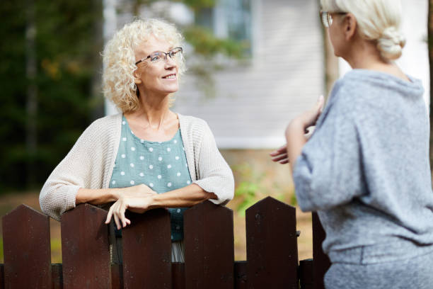 Consulting with neighbour Two mature female neighbours talking through fence about everyday life stuff neighbour stock pictures, royalty-free photos & images