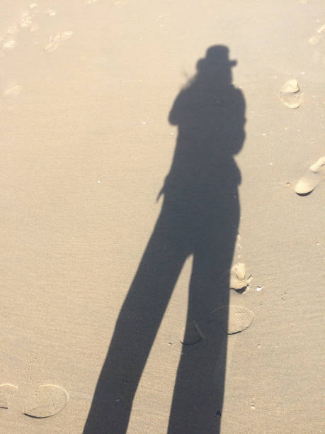 istock on the beach on a summers day, shadow with sun hat with footprints in the background 1054966148