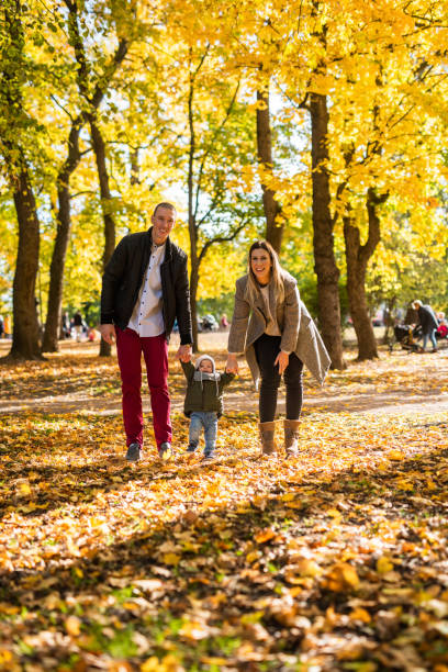 madre e padre all'aperto insegnano al bambino a camminare. - baby first steps autumn child foto e immagini stock