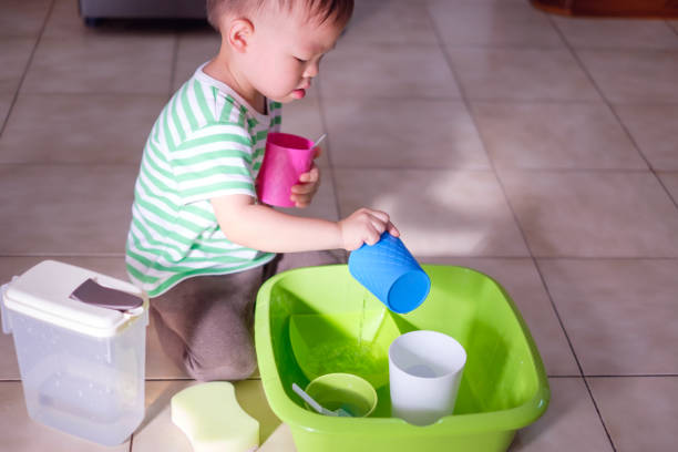 Cute little Asian 18 months old toddler boy child having fun pouring water into cup, Wet Pouring Montessori Preschool Practical Life Activities stock photo