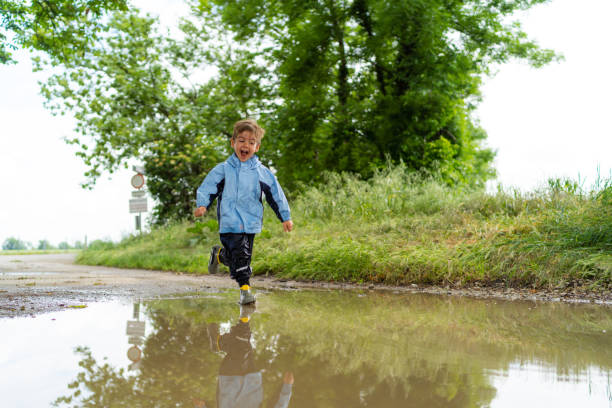 istock happy little boy running through rain puddle 1054967724