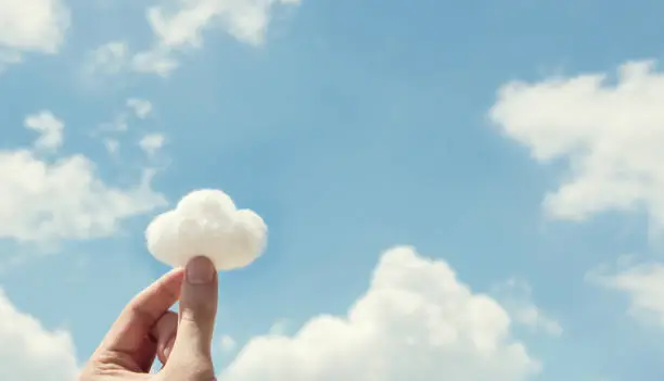 Photo of Woman hand holding cotton wool on cloud sky background. The development of the imagination.