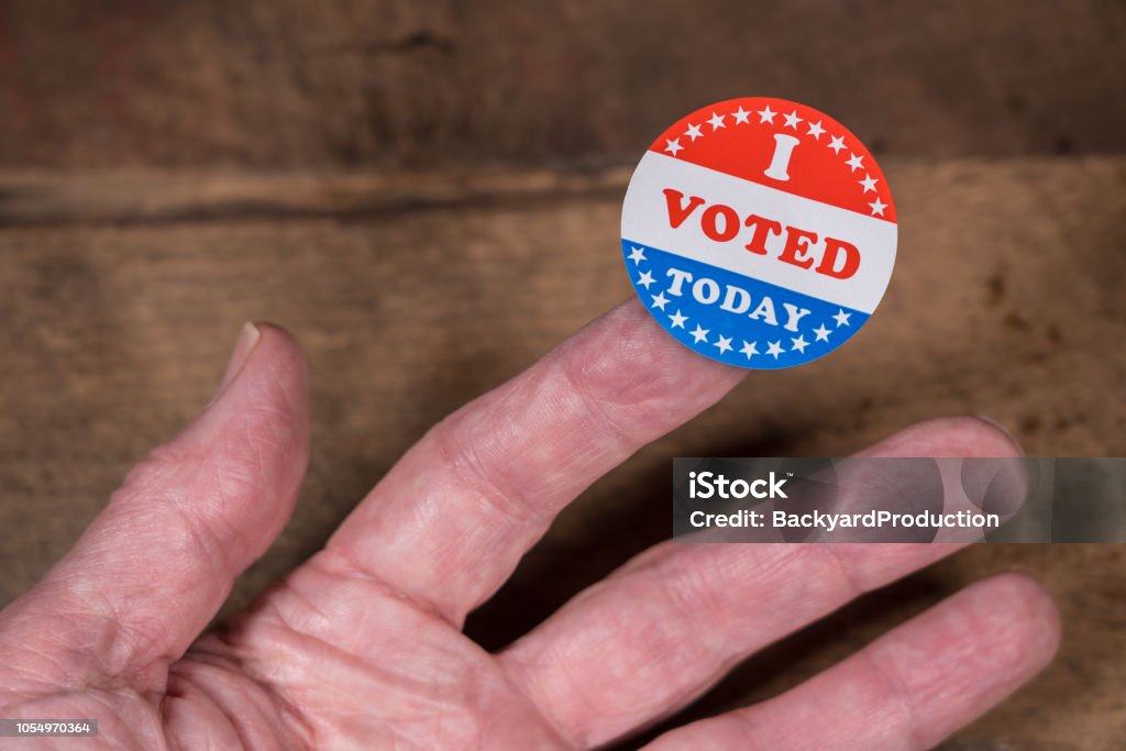 I Voted Today paper sticker on mans finger on rustic wooden table I Voted Today sticker on senior caucasian mans finger on rustic rural wooden table Voting Stock Photo