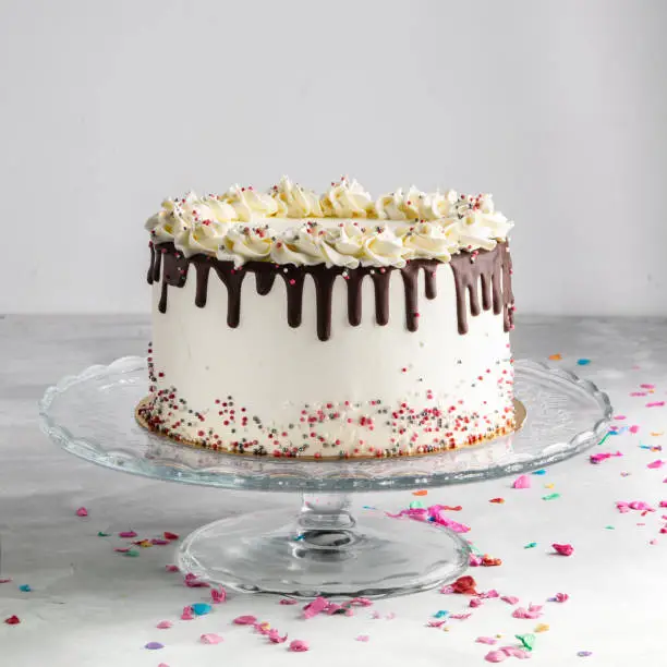 Birthday Drip Layered Cake with chocolate ganache and sprinkles on a white background with party decor. Horizontal. Copy space. Celebration concept. Trendy Drip Cake.