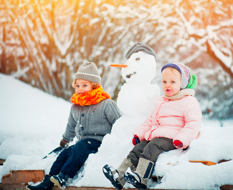 Boy and Girl sitting near the Snowman and Enjoying Winter