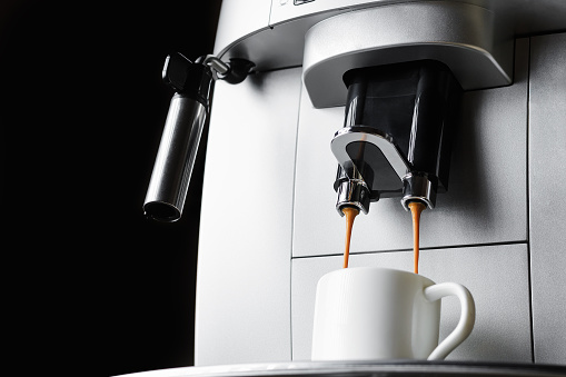 Modern coffee machine brews espresso coffee in white cup, close up