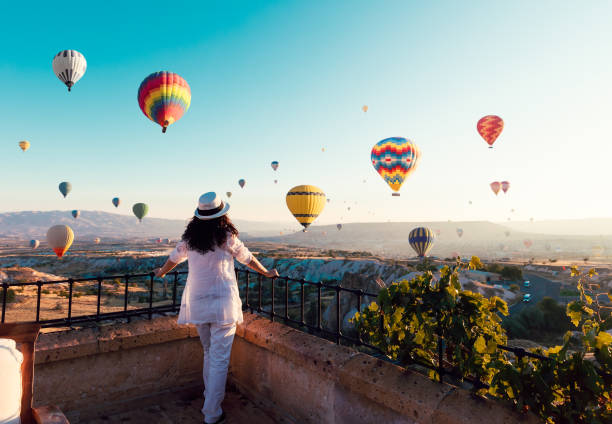 belle femme asiatique je regarde coloré montgolfières volant au-dessus de la vallée à cappadocia, décor de conte de fées turquie.turquie cappadoce des montagnes. turquie cappadoce féerique paysage de montagnes. - ballooning festival photos et images de collection