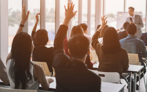 istock aised up hands and arms of large group in seminar class room 1054986454