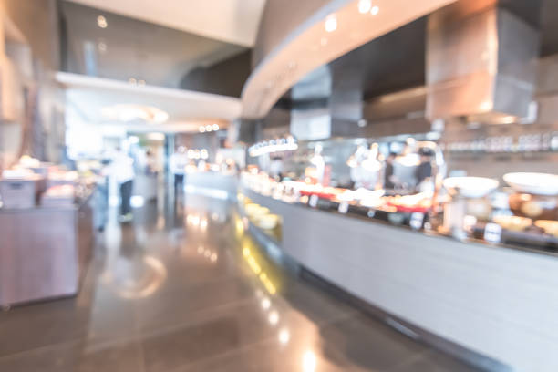 istock Buffet at hotel restaurant interior blur background with blurry open kitchen counter bar of food catering service business with chef staff cooking for breakfast, lunch or dinner meal 1054987782