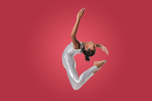 Beautiful gymnast athlete teenage girl doing exercise jumping in studio on colored background