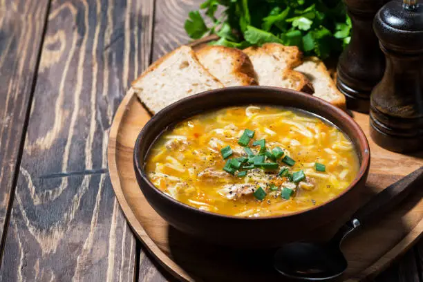 chicken soup with egg noodles on wooden background, horizontal