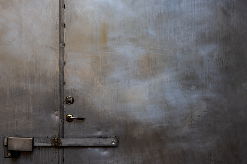 Closeup of closed scratched grungy shiny steel door with locks and handle outdoor. Horizontal composition.