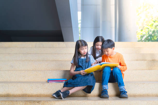 屋外の階段に座っている間に一緒に本を読むかわいいアジアの子供たち - staircase steps education stone ストックフォトと画像