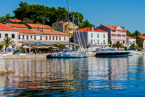 Sali, Croatia - October 04, 2018: Sailing boats anchor in front of Maritimo restaurant in Town Sali on Adriatic coast. It is nice sunny day without wind and tourists are walking from sailing boat to the restaurant. Sali is on Long Island (Dolgi otok) what is in central Dalmatia coast not far from big Town Zadar on Croatian mainland, Adriatic sea as part of  Mediterranean.