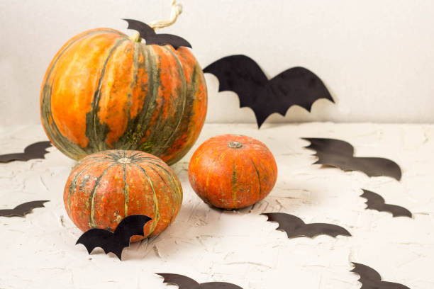 istock orange pumpkin and paper bats on white table, halloween concept 1054999612