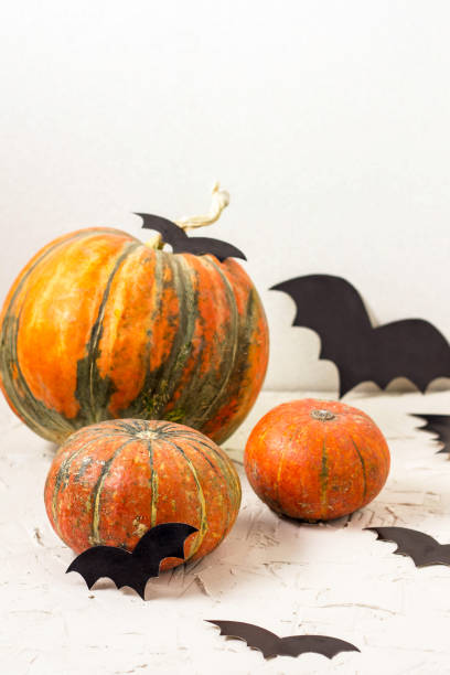 istock orange pumpkin and paper bats on white table, halloween concept 1054999636