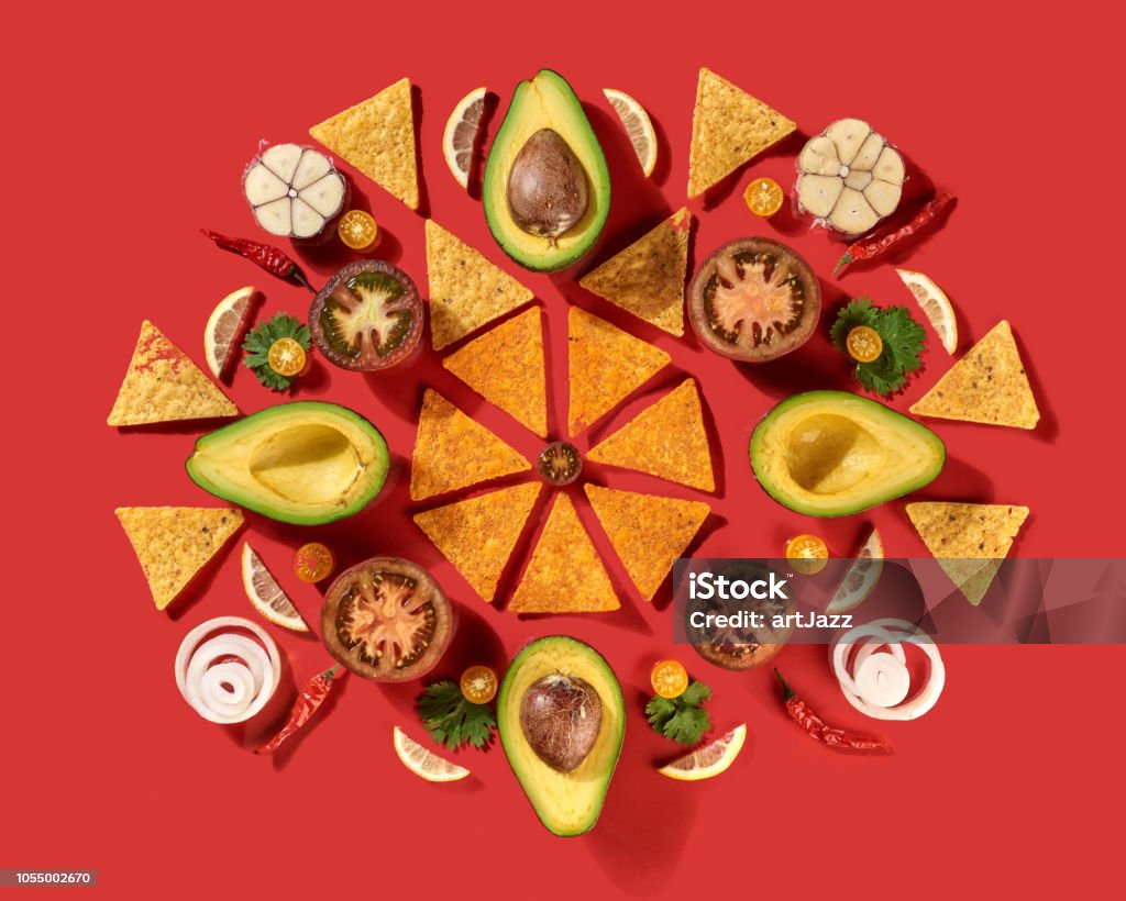 Mexican corn nachos chips, avocado, lemon, garlic, tomato, onion, parsley green as a round pattern - ingredients for tomato chili sauce on a red background. Top view. Round traditional mexican pattern with corn nachos chips, fresh natural fruits, vegetables, spices, chilli greens - ingredients for Guacamole dressing on a red background. Flat lay. Mexico Stock Photo