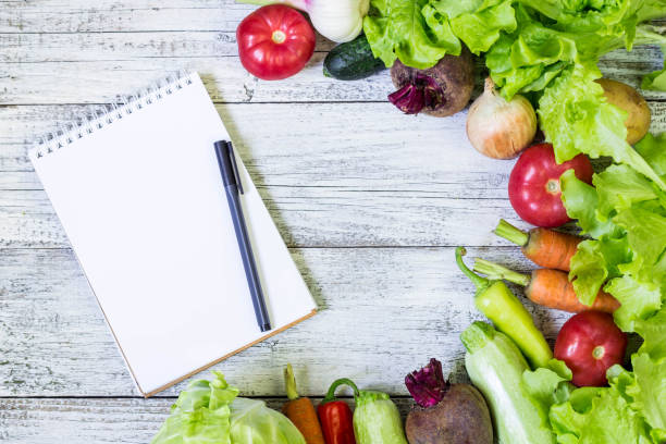 istock Fresh juicy vegetables border, blank white notepad with copy space and pen on white wooden background, top view. 1055003262
