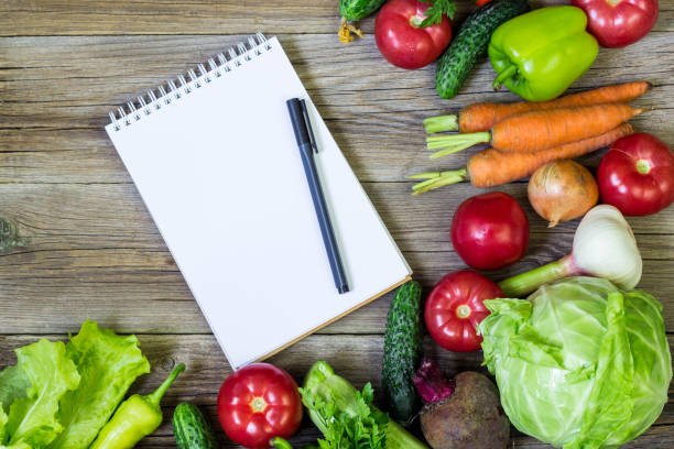 istock Fresh juicy vegetables border, blank white notepad with copy space and pen on wooden background, top view. 1055003322