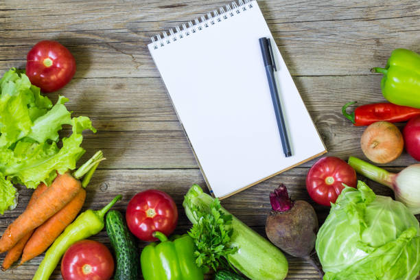 istock Fresh juicy vegetables border, blank white notepad with copy space and pen on wooden background, top view. 1055003338