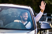 Happy businessman driving a car and waving to someone.