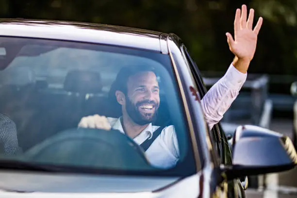 Photo of Happy businessman driving a car and waving to someone.