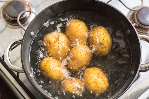 Potatoes boiling in a saucepan on a gas hob.