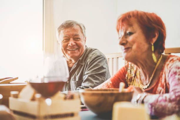 happy mature people eating and laughing at home dinner - senior friends having fun drinking red wine and talking about funny things - joyful elderly lifestyle concept - focus on man face - couple restaurant day south america imagens e fotografias de stock