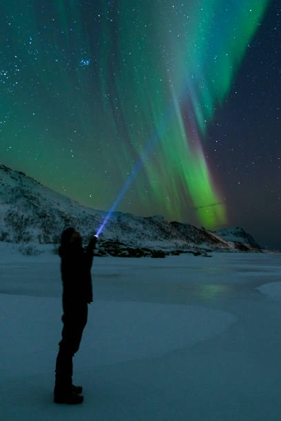 istock Man with a flashlight looking at Northern Lights, Aurora Borealis over the Lofoten 1055014690