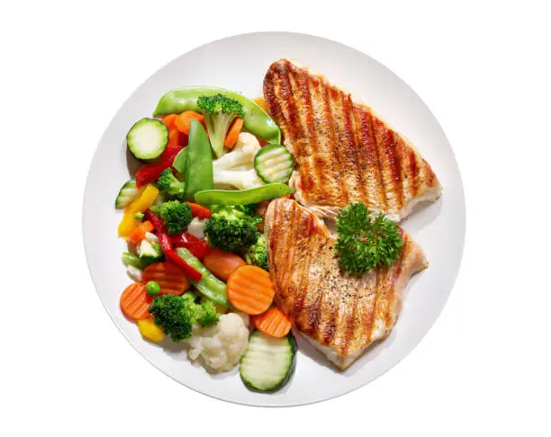 Photo of plate of grilled chicken with vegetables on wite background, top view