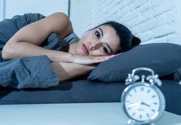 Sleepless and desperate beautiful latin woman awake at night not able to sleep looking at clock suffering from insomnia in sleep disorder concept. stock photo