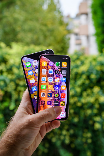 PARIS, FRANCE - OCT 2, 2018: Proud man customer POV comparing the new latest iPhone Xs and Xs Max smartphones telephones after the unboxing against green outdoor city background