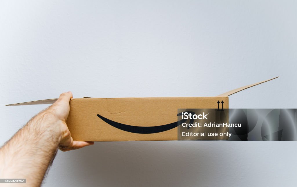 Amazon cardboard box against white background in hand PARIS, FRANCE - AUG 11, 2018: Man holding against white background freshly unboxed Amazon Prime cardboard box Amazon Prime Stock Photo