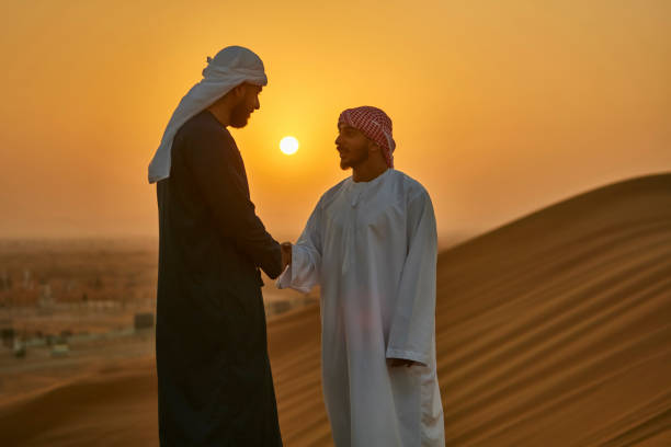 hommes du moyen-orient se serrant la main au lever du soleil dans le désert - middle eastern ethnicity sheik wealth men photos et images de collection