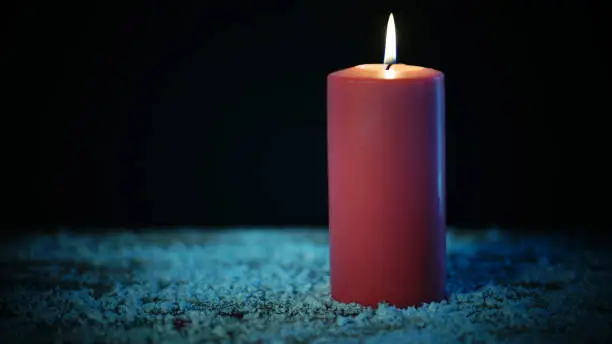 Red Christmas candle glowing on the ground with golden light in dark background