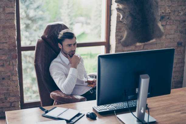 bem sucedido conceito de lazer. vista de alto ângulo superior de espírito homem pensativo com roupa formal, sentado na cadeira de conforto em frente a tela pc bebida conhaque conhaque uísque ou rum bebida na luz interior - high minded - fotografias e filmes do acervo