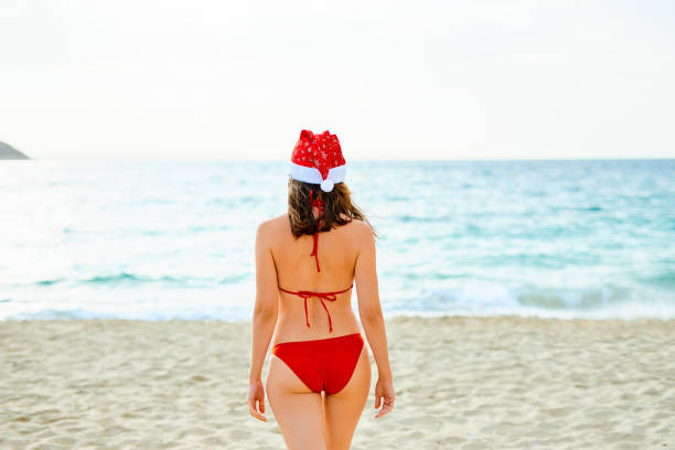 istock Young woman is strolling on the beach wearing Santa hat 1055031454