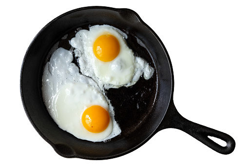 Two fried eggs in cast iron frying pan isolated on white from above.