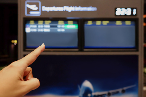 Close up shot of female hands pointing her finger showing delay flight on departure flight information board