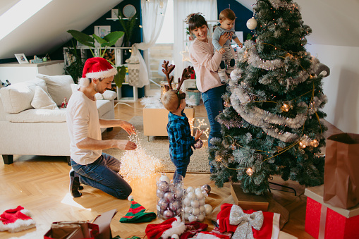 Photo of a cute little family with two children, decorating Christmas tree.