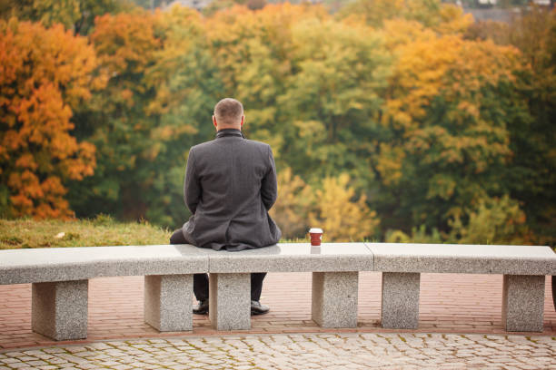 Lone man sitting on the stone bench and looking at nature. Back view.