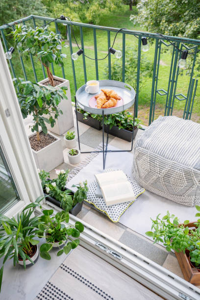 istock Beautiful space for meal and relaxation on a green balcony with a comfy ottoman, string lights and a tray with sweet pastries and coffee 1055048580