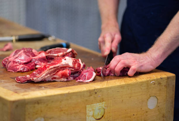Local Butcher preparing beef on a butchers block. Cutting into cubes for a stew