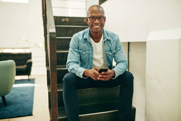istock Smiling African businessman sitting on office stairs using a cellphone 1055067450