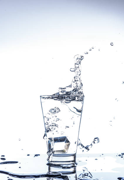 istock Ice dropping and water splashing in the glass with reflection on the mirror table and isolated on white background. 1055074936