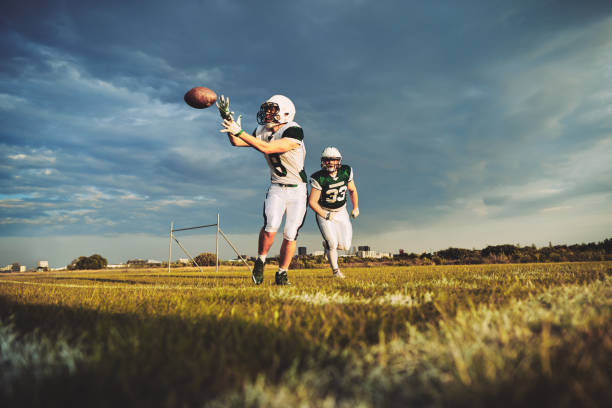 American football player catching a pass during team drills American football player receiving a pass during a team practice on a football field against a moody afternoon sky reception american football photos stock pictures, royalty-free photos & images