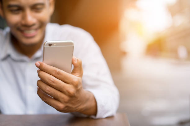 istock close up asian man holding smartphone for watching video streaming on web or surfing internet or play social media with happy feeling (smiling) after hard working , lifestyle people nowadays concept 1055083164
