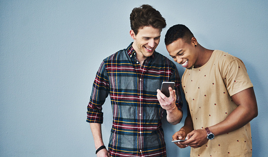 Studio shot of two young men using a mobile phone together against a gray background