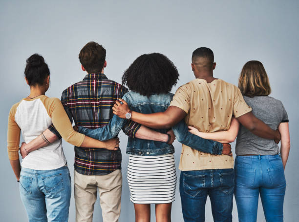 Good friends support one another Rearview studio shot of a diverse group of young people embracing each other against a gray background arm around stock pictures, royalty-free photos & images